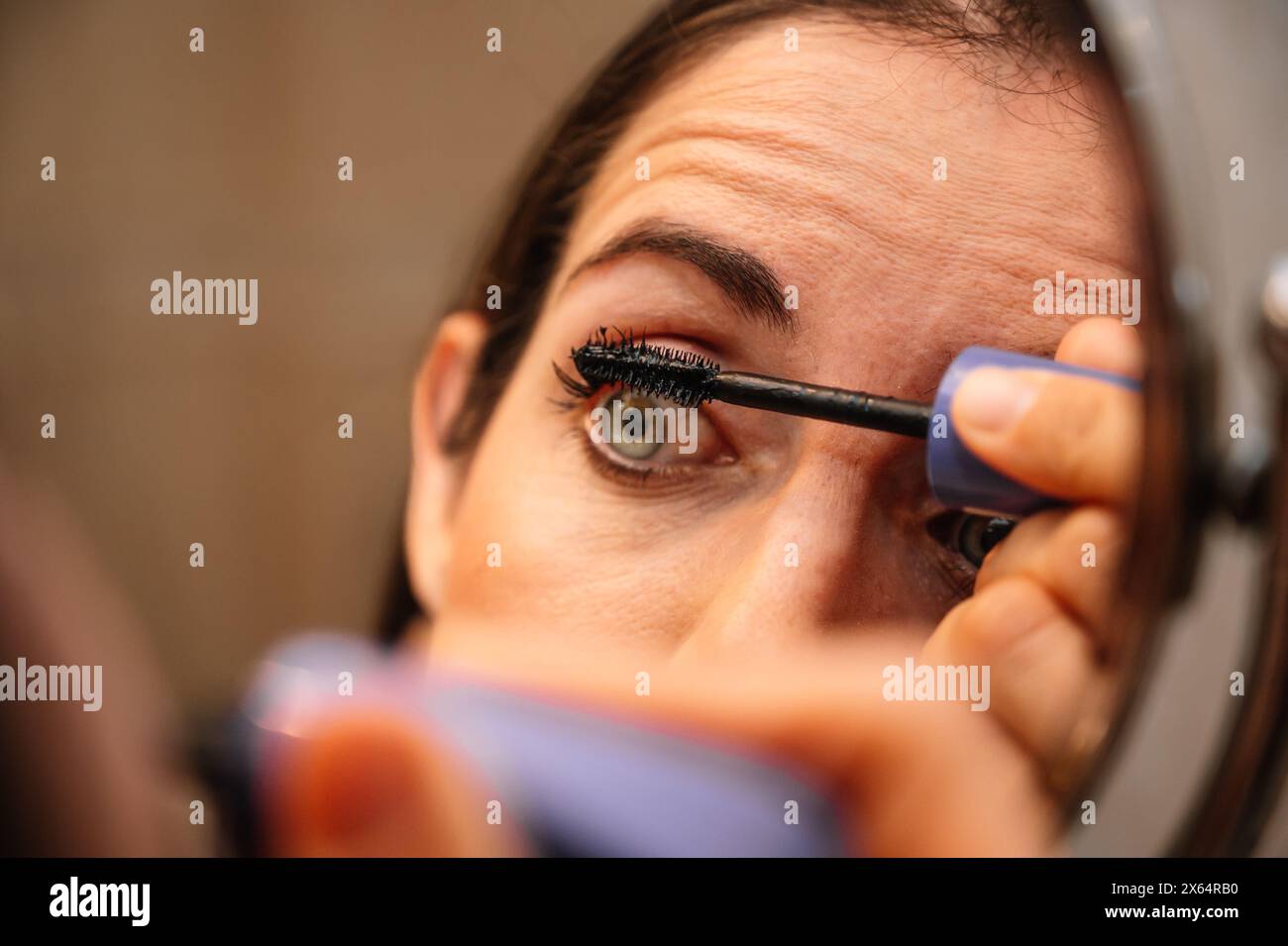 Una donna sta applicando il mascara agli occhi. Si sta guardando in uno specchio. Concetto di cura personale e cura del corpo Foto Stock