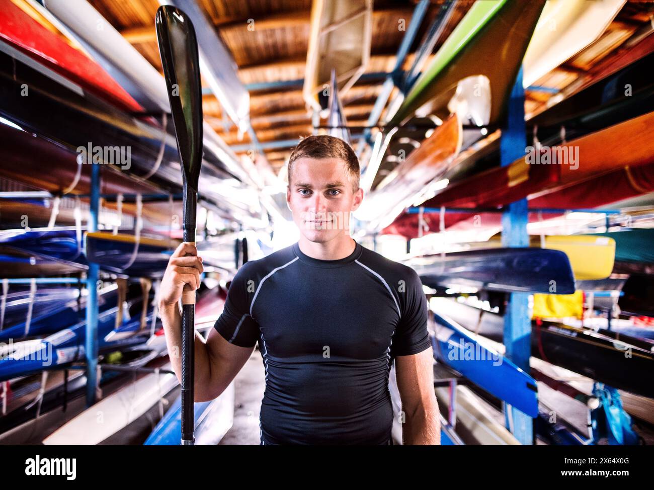 Portrat di giovane canoista in piedi nel mezzo di canoe impilate. Concetto di canoa come sport dinamico e avventuroso Foto Stock