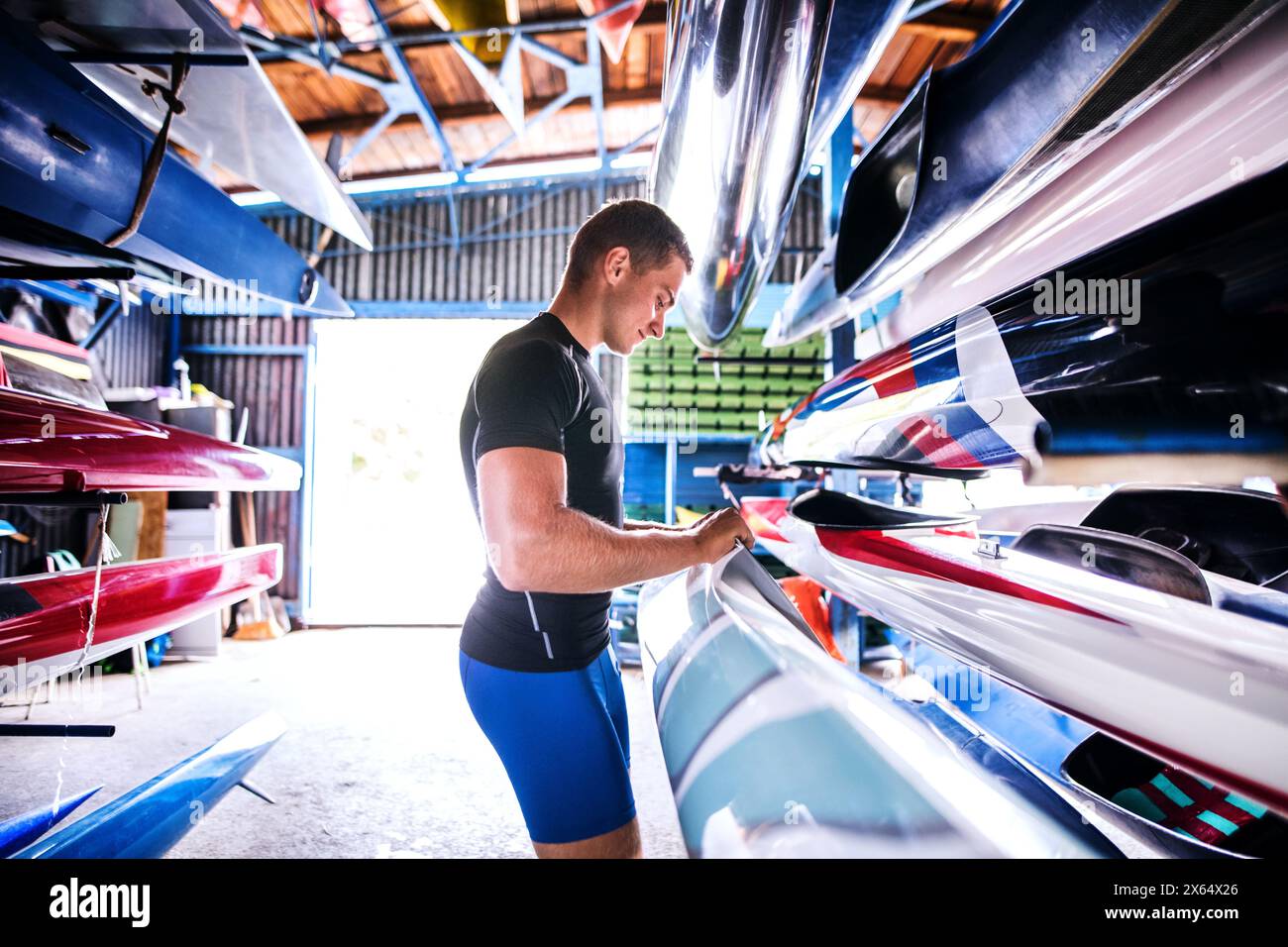 Portrat di giovane canoista in piedi nel mezzo di canoe impilate. Concetto di canoa come sport dinamico e avventuroso Foto Stock