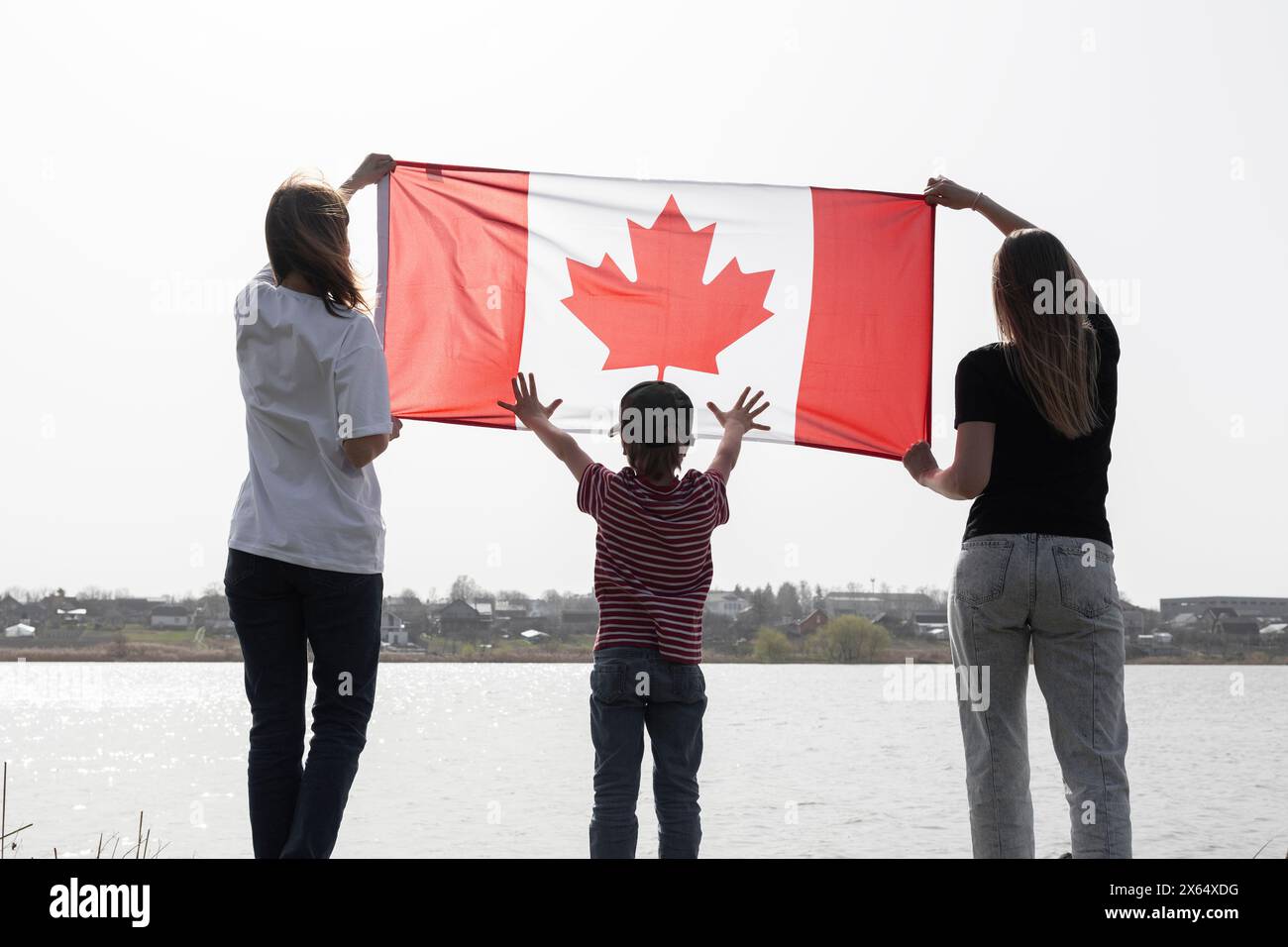 La famiglia di tre persone detiene la bandiera canadese. Un uomo, una donna e un bambino in piedi con la schiena con una grande bandiera canadese in natura. Viaggi, immigrazione. H Foto Stock