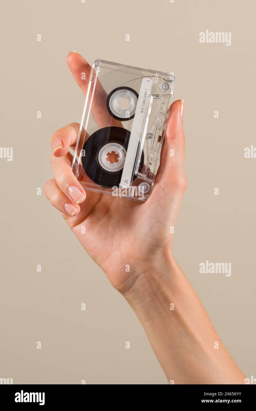 Crop Anonymous Woman che mostra un concetto di musica retrò vintage compact cassette con sottofondo beige Foto Stock