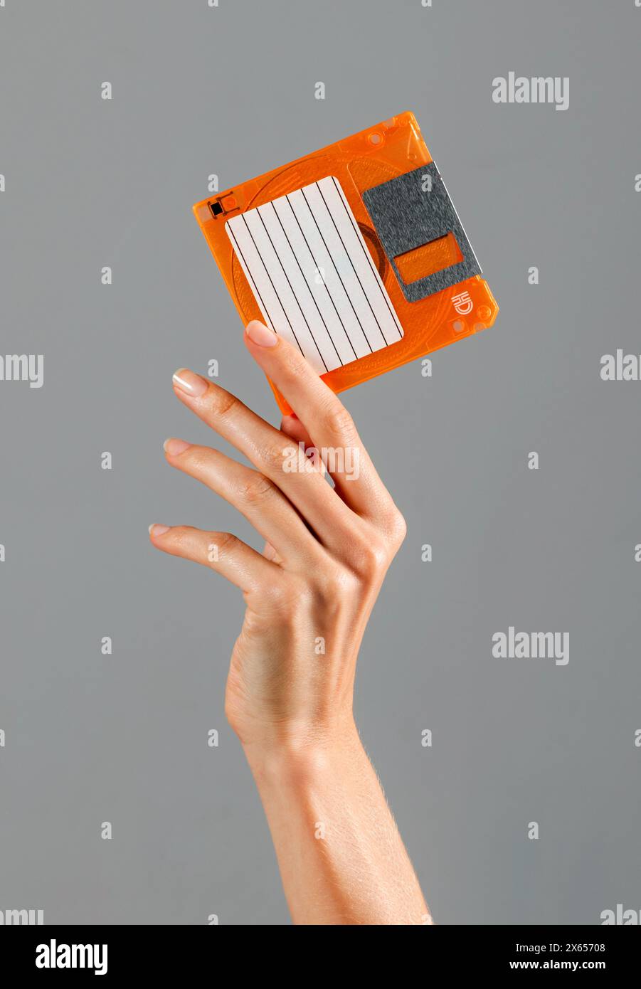 Ritaglia la mano femminile che mostra un floppy disk retro di colore arancione su sfondo grigio in studio Foto Stock