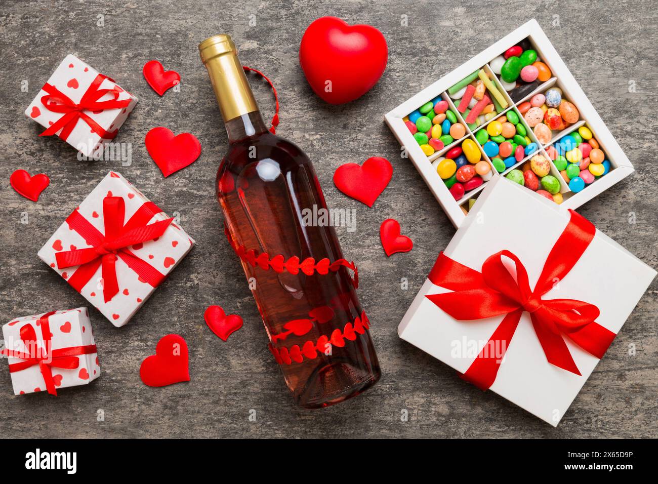 Bottiglia di vino rosso su sfondo colorato per San Valentino con regalo e cioccolato. A forma di cuore con scatola di cioccolatini in omaggio vista dall'alto e spazio per fotocopie. Foto Stock