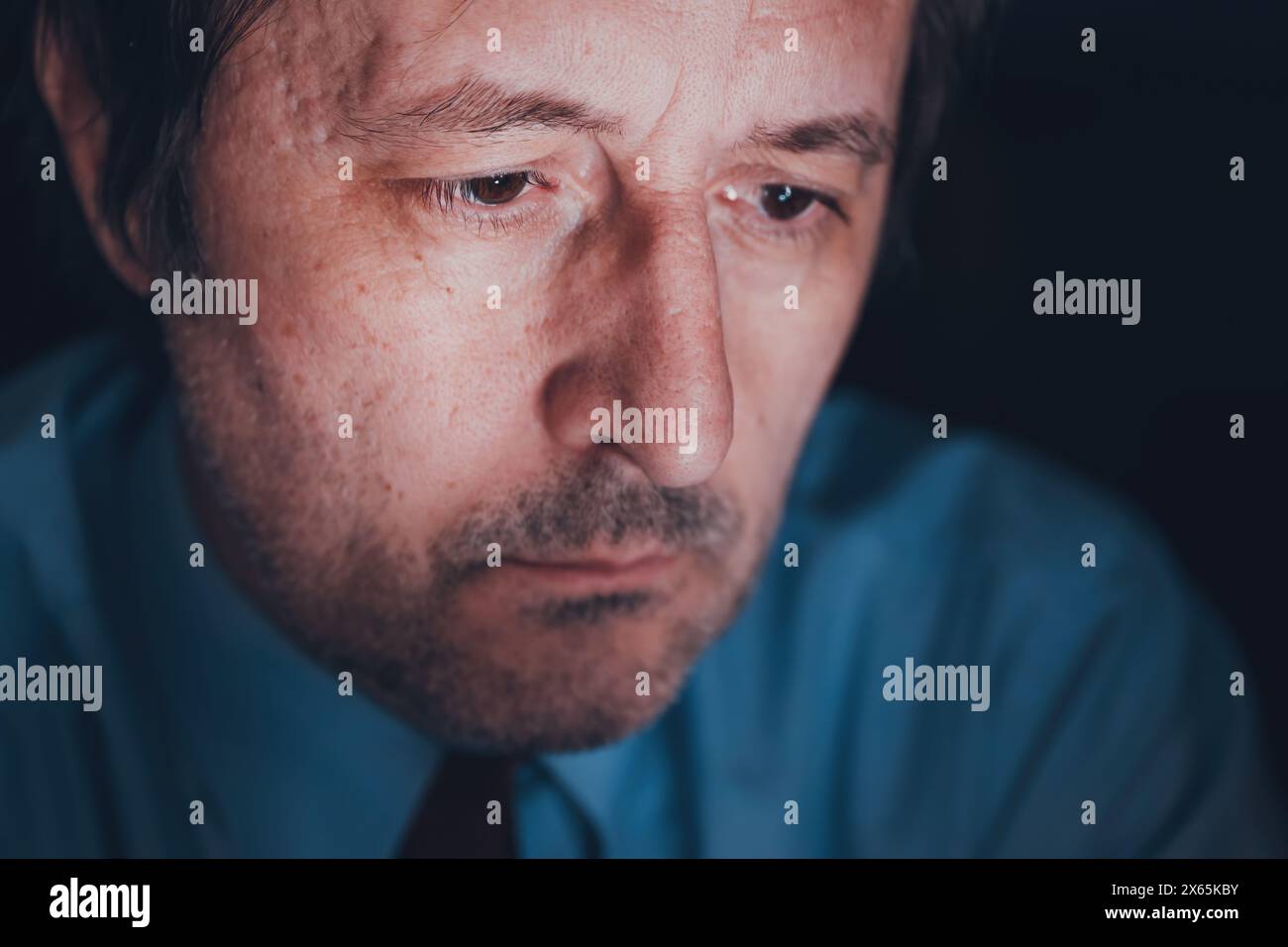 Concetto di affaticamento dello schermo, volto di un uomo d'affari adulto illuminato dalla luce dello schermo del dispositivo mobile a tarda notte, messa a fuoco selettiva Foto Stock