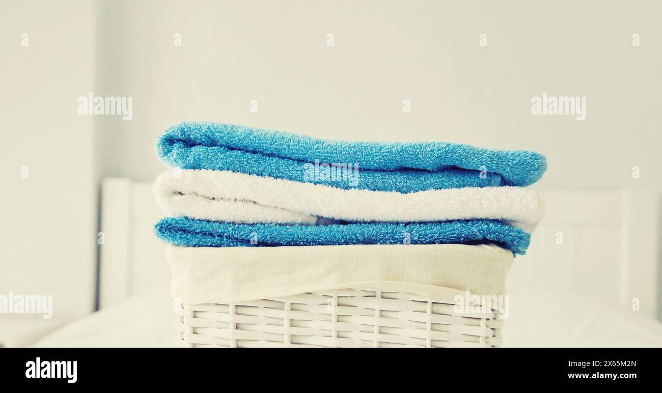 Cestino per bucato in vimini con asciugamani piegati puliti sul letto Foto Stock