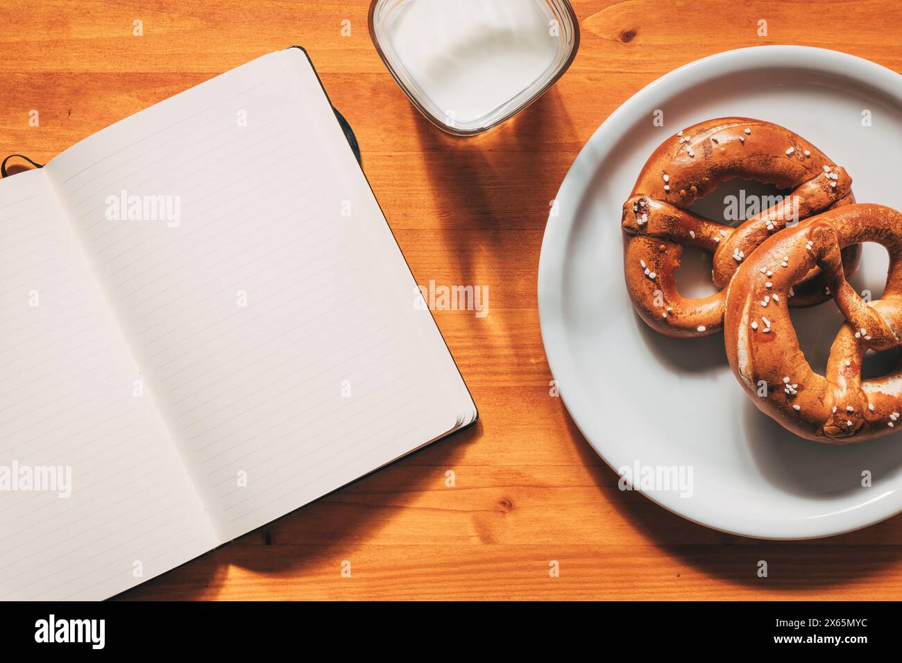 Pretzel e yogurt a colazione, cibo e quaderno vuoto sul tavolo, vista dall'alto Foto Stock