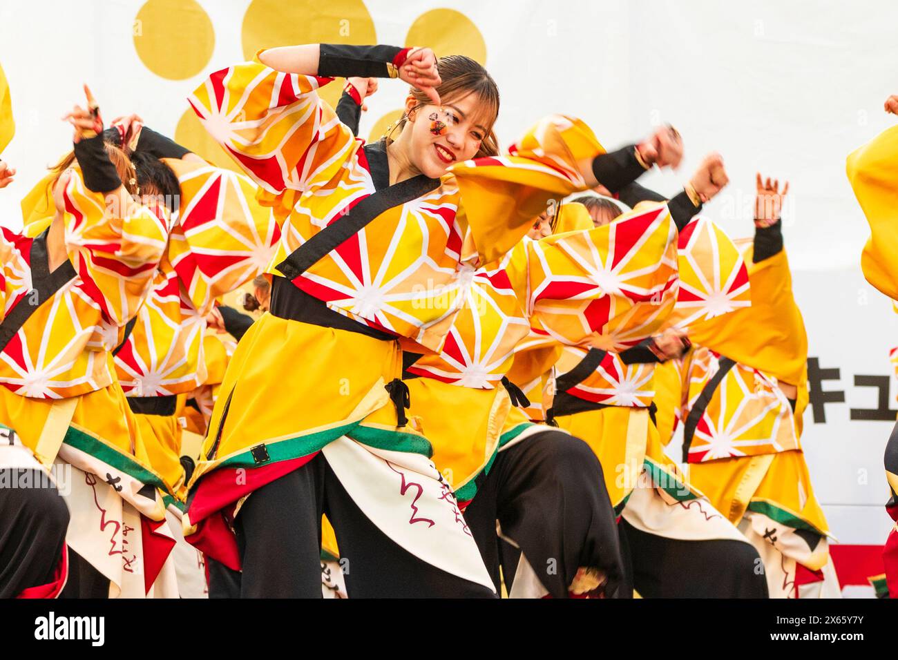 Gruppo di ballerine Yosakoi adolescenti che ballano con tuniche gialle luminose yukata con maniche lunghe durante il festival di danza Kumamoto Kyusyu Gassai Foto Stock