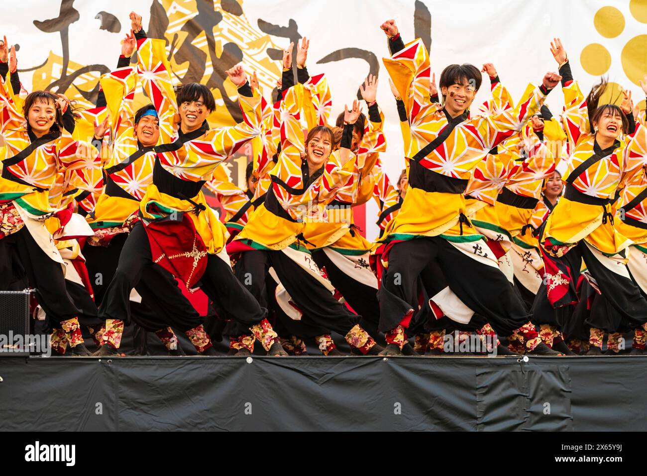 Gruppo di ragazzi e donne ballerini Yosakoi che ballano con tuniche gialle luminose yukata con maniche lunghe durante il festival Kumamoto Kyusyu Gassai. Foto Stock