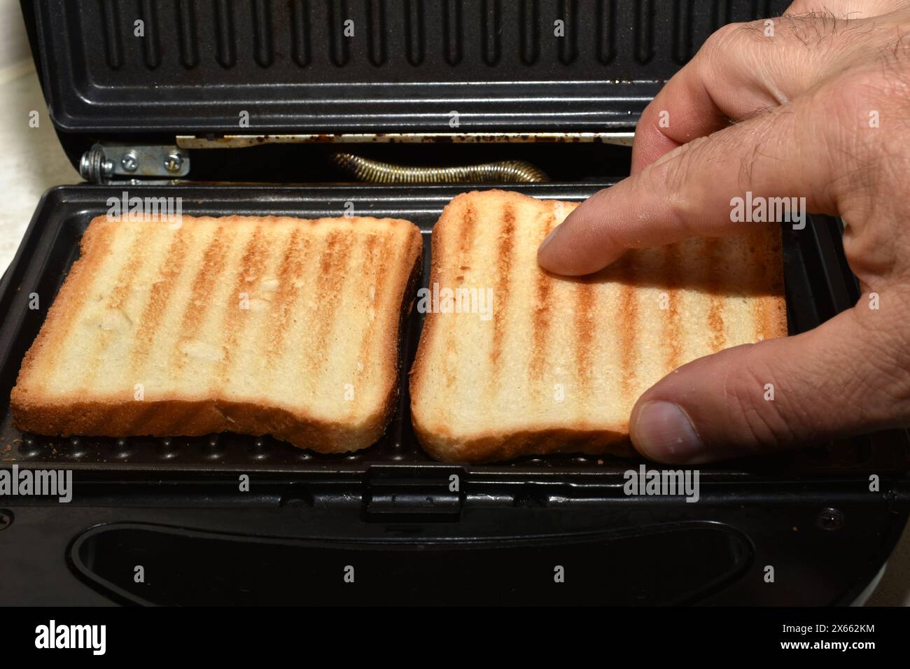 La mano di un uomo rimuove dal grill pane e toast già cotti. Foto Stock