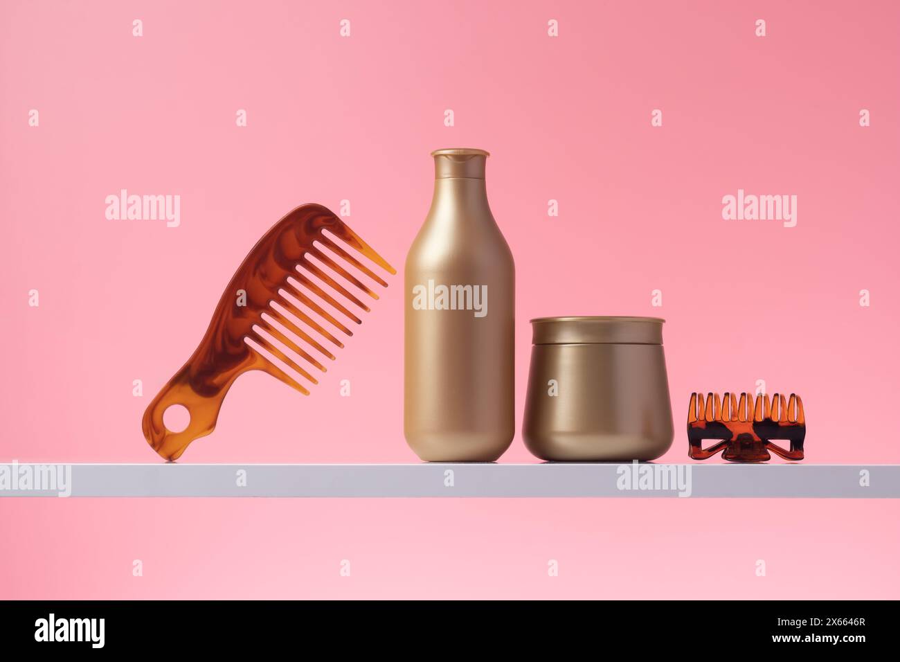 Shampoo e balsamo per capelli, vari prodotti per la cura dei capelli su ripiano nel bagno domestico, sfondo rosa. Pettine e bottiglie in plastica dorata in bagno, conf Foto Stock
