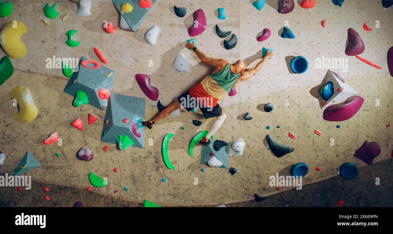 Forte esperto arrampicatore che pratica arrampicata in solitaria sul muro di Bouldering in una palestra. Uomo che fa esercizio presso la palestra Indoor fitness Facility, praticando sport estremi per il suo sano allenamento Lifestyle. Sparato da dietro. Foto Stock