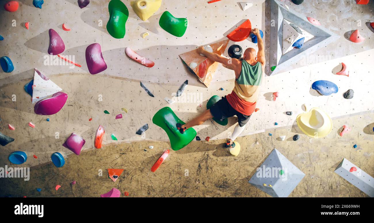 Forte esperto arrampicatore che pratica arrampicata in solitaria sul muro di Bouldering in una palestra. Uomo che fa esercizio presso la palestra Indoor fitness Facility, praticando sport estremi per il suo sano allenamento Lifestyle. Sparato da dietro. Foto Stock