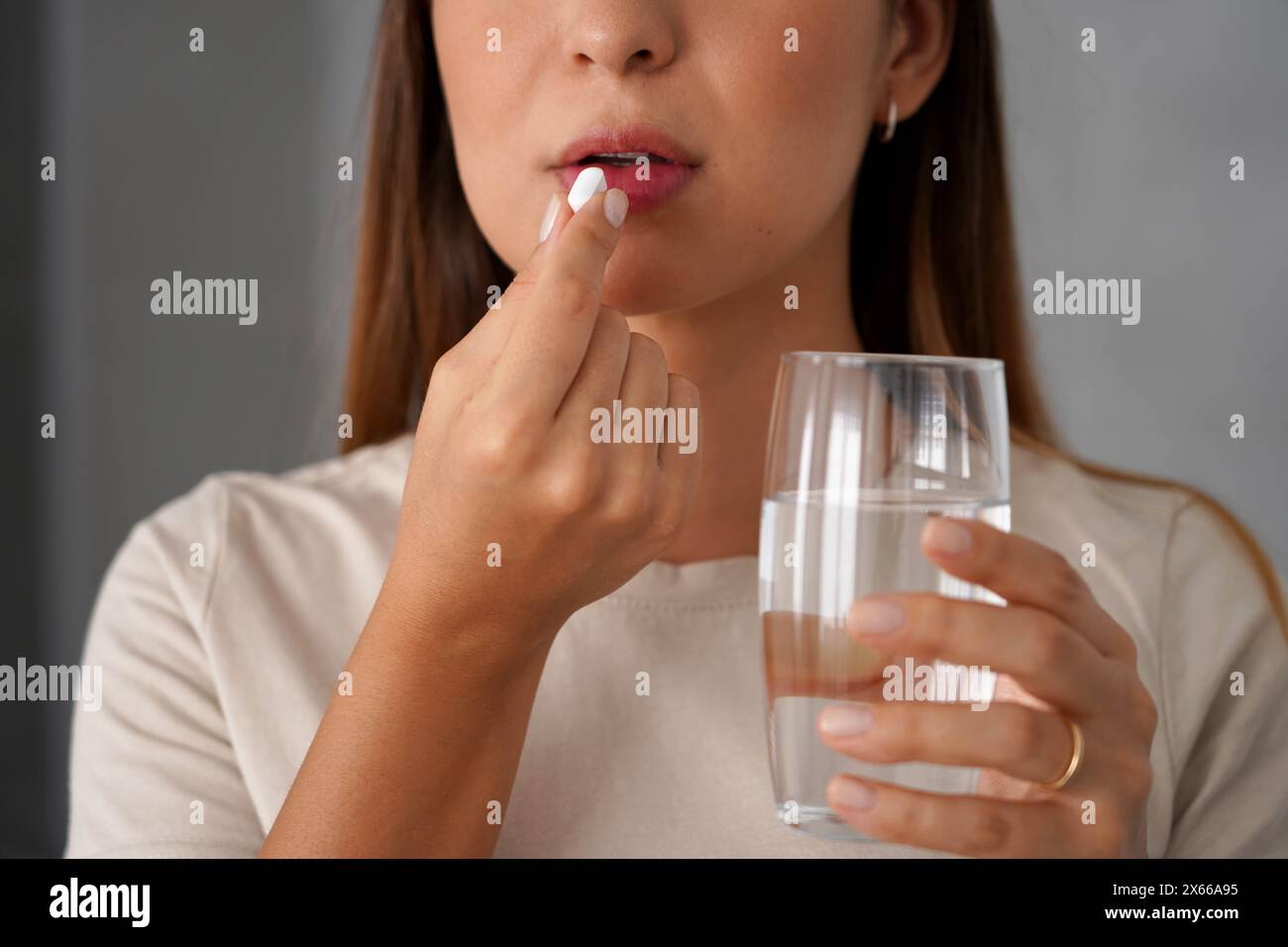 Una giovane donna prende una pillola mentre tiene in mano un bicchiere d'acqua Foto Stock