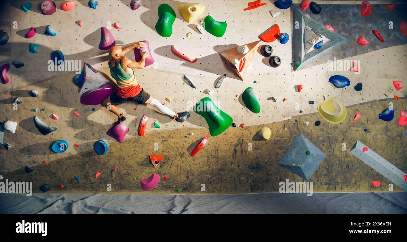 Forte esperto arrampicatore che pratica arrampicata in solitaria sul muro di Bouldering in una palestra. Uomo che fa esercizio presso la palestra Indoor fitness Facility, praticando sport estremi per il suo sano allenamento Lifestyle. Sparato da dietro. Foto Stock