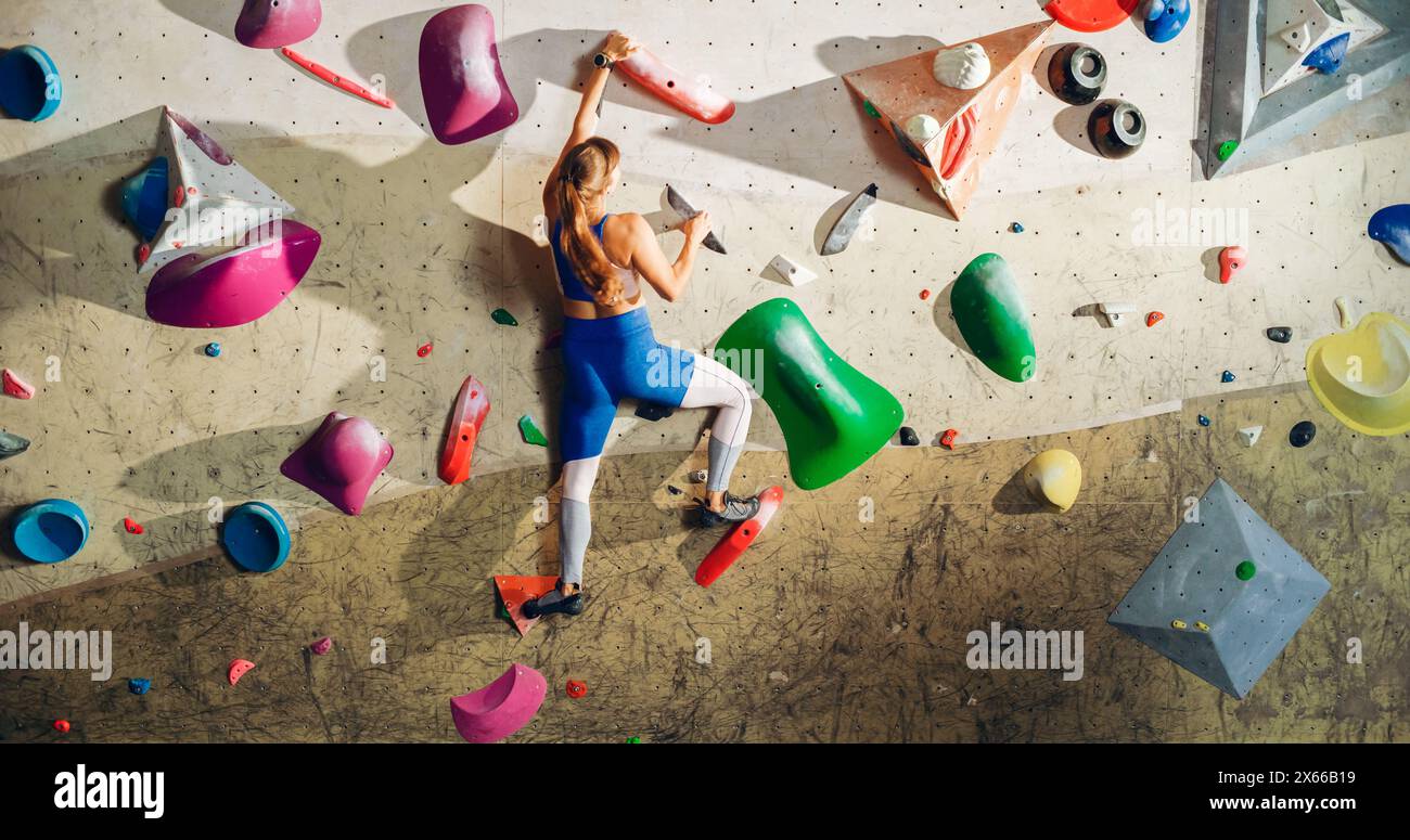 Atletica Rock Climber che pratica l'arrampicata in solitaria sul muro di Bouldering in palestra. Esercizio fisico femminile presso la palestra Indoor fitness, facendo sport estremi per il suo sano allenamento Lifestyle. Sparato da dietro. Foto Stock