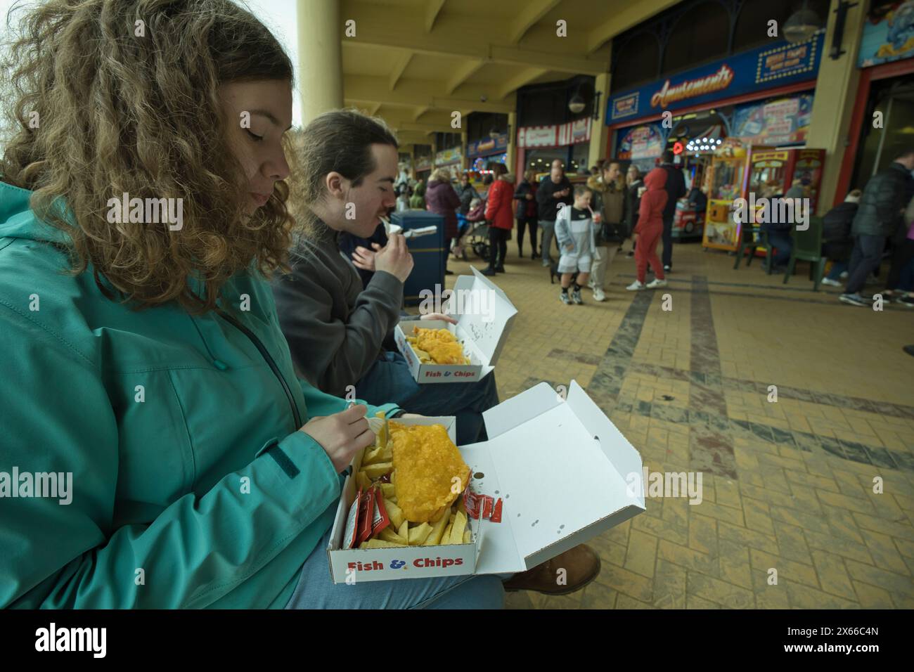 Giovani adulti che mangiano fish and chips nella spiaggia di Whitmore Bay a Barry Island in Galles all'inizio della primavera Foto Stock