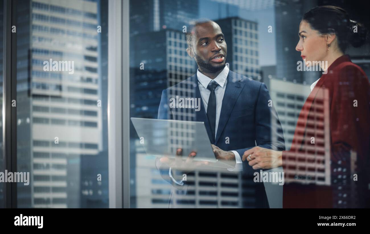 Ritratto di un CEO aziendale e Investment Manager di successo che parla, utilizzando un computer portatile mentre si trova in un ufficio cittadino. Due uomini d'affari di successo si sono confrontati con il software e-Commerce. Colpo esterno Foto Stock