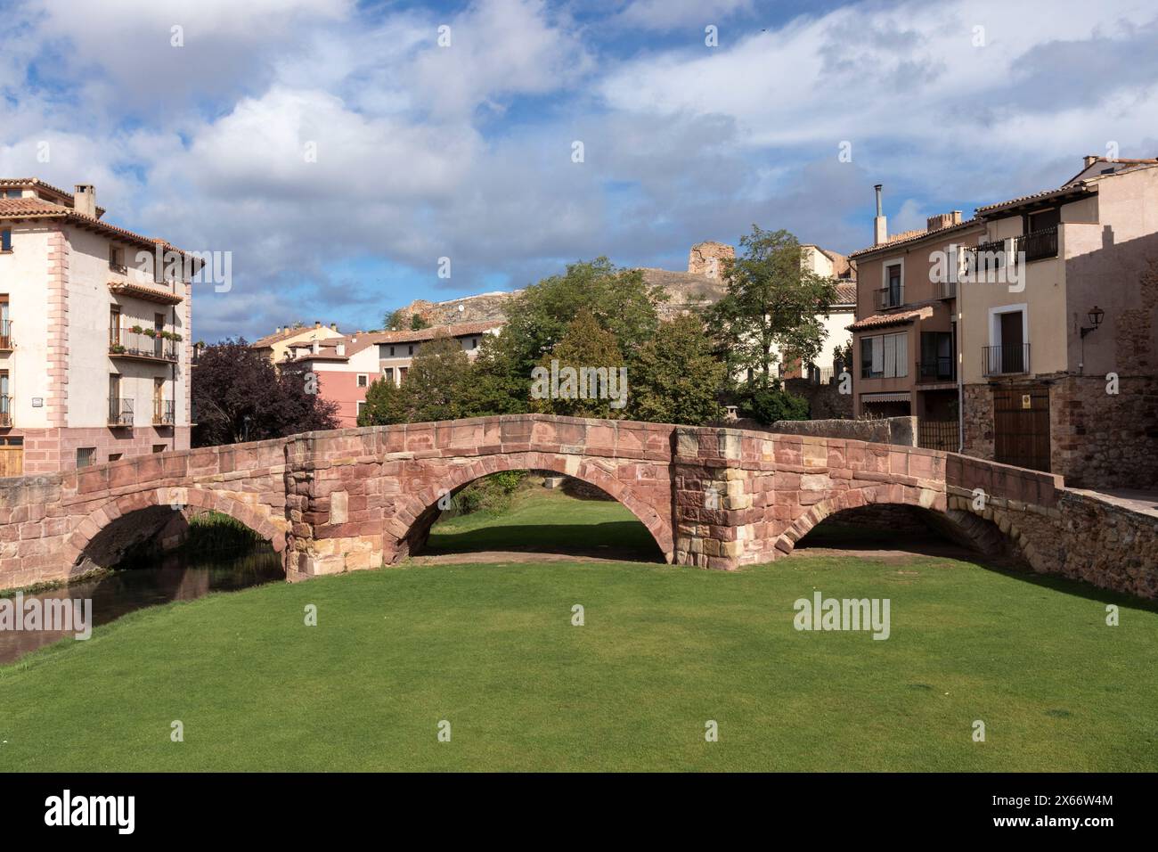 il ponte di pietra si estende su un'area verde, collegando case pittoresche sotto un cielo parzialmente nuvoloso in un ambiente storico Foto Stock