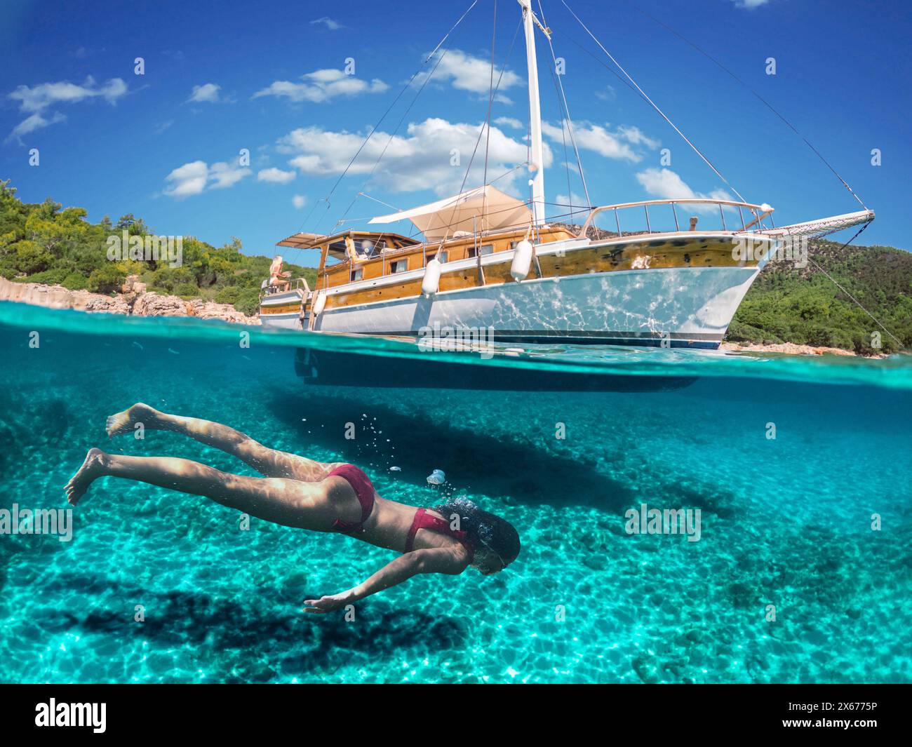 Donna subacquea sta facendo snorkeling su una bellissima spiaggia di mare. La metà inferiore del quadro è occupata dal fondale marino, in alto - la costa con uno yacht e. Foto Stock