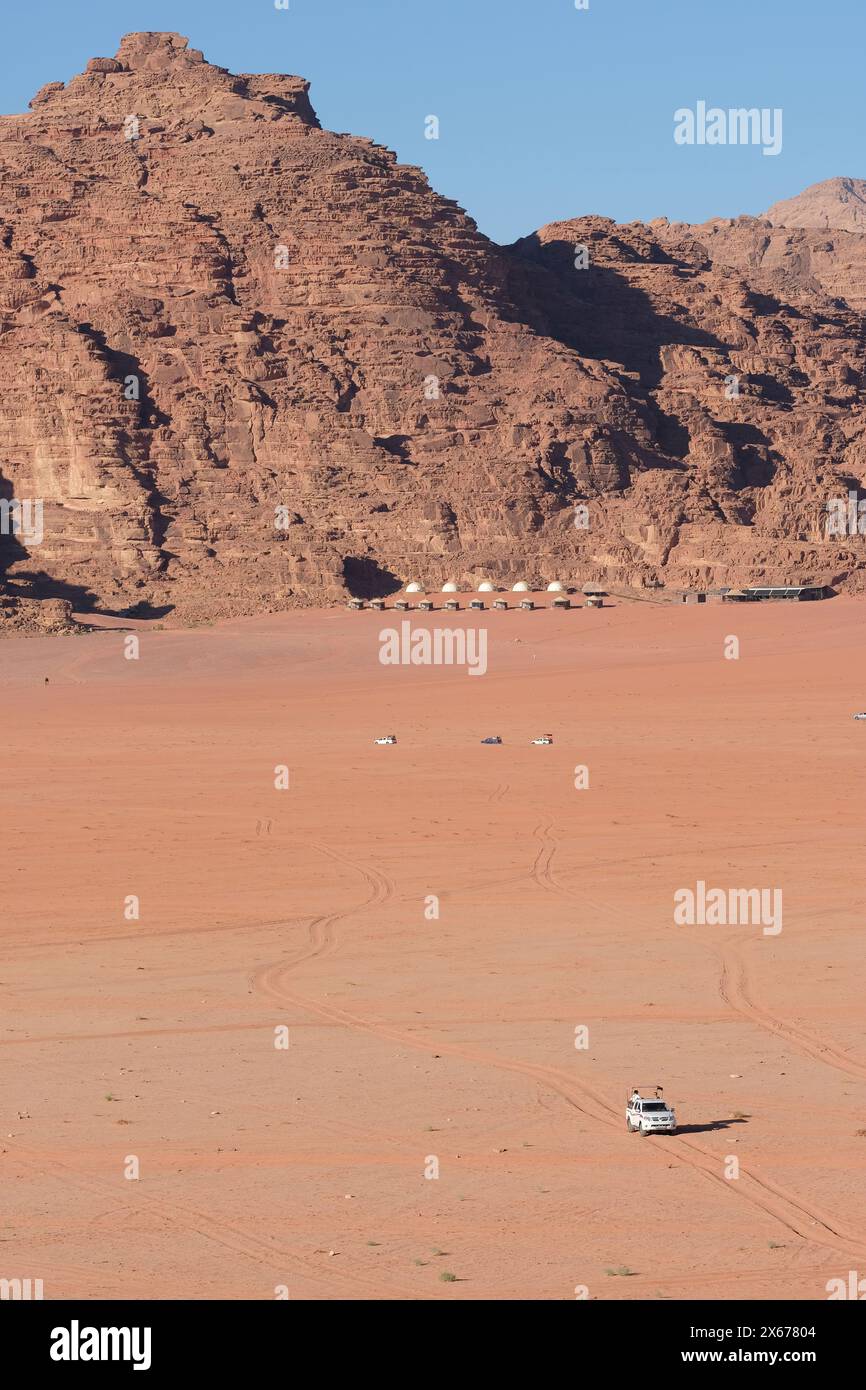 Wadi Rum, Giordania - un veicolo 4x4 attraversa il vasto deserto remoto con un lussuoso accampamento turistico sullo sfondo - foto agosto 2023 Foto Stock