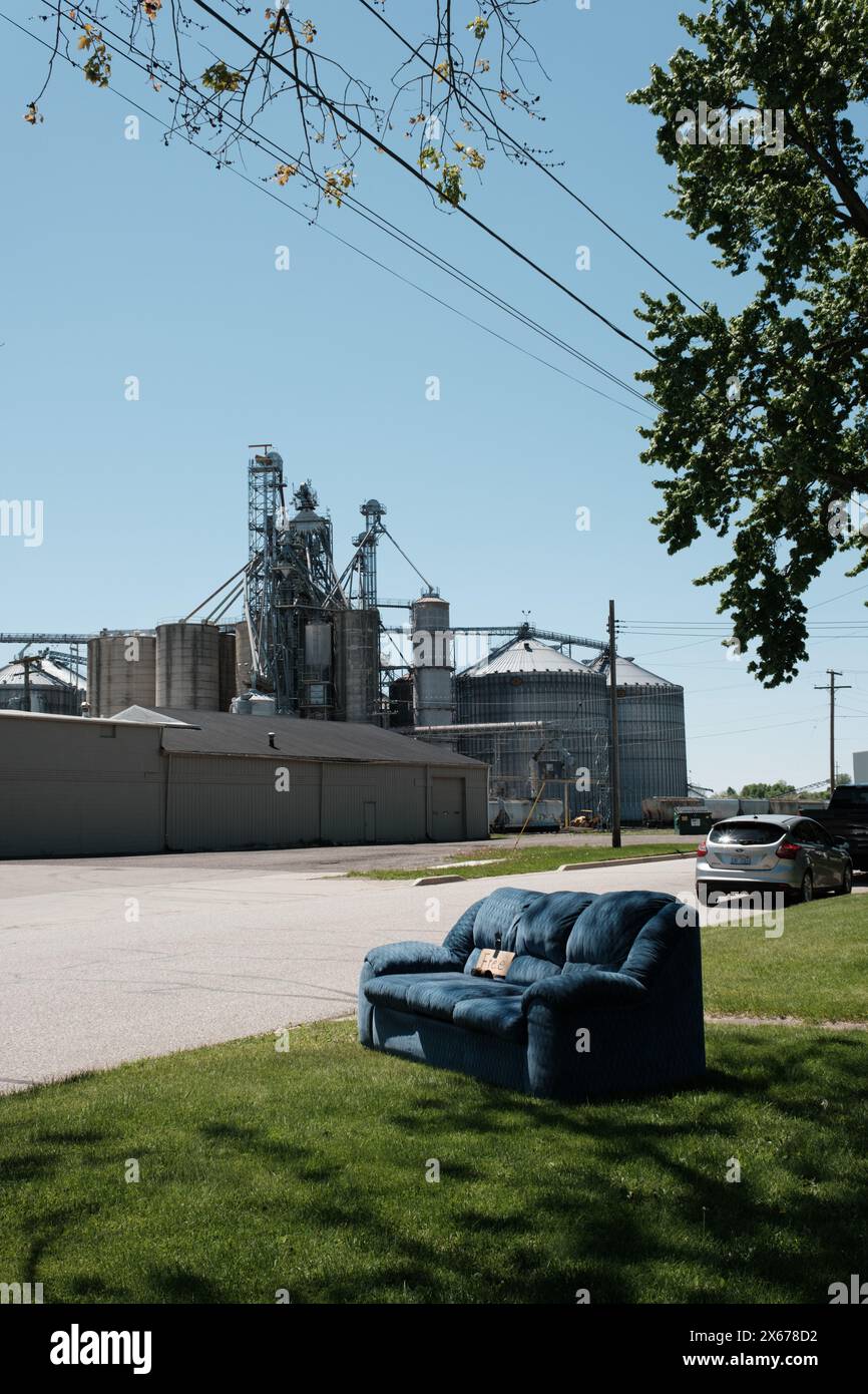 Un divano blu viene regalato su un prato, con lo stabilimento industriale Michigan Agricultural Commodities sullo sfondo, Marlette Michigan USA Foto Stock