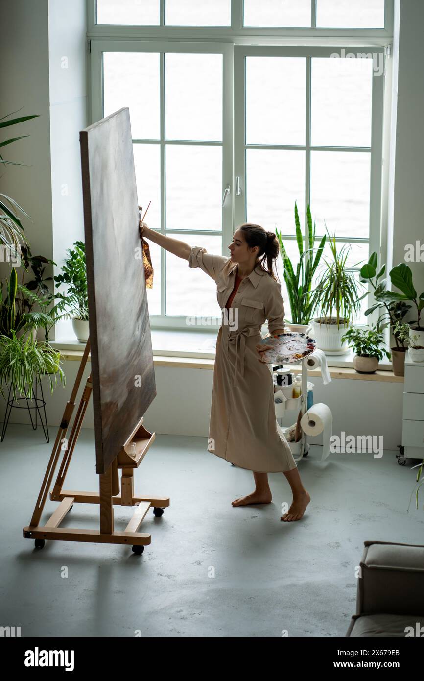 Donna seria pittrice in studio d'arte che crea capolavoro su grande tela. Lavoro artistico creativo Foto Stock