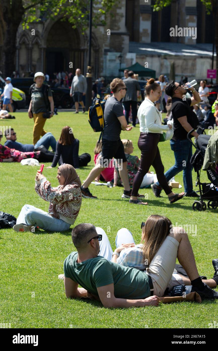 La gente gode del caldo sole in Parliament Square, Londra. Foto Stock