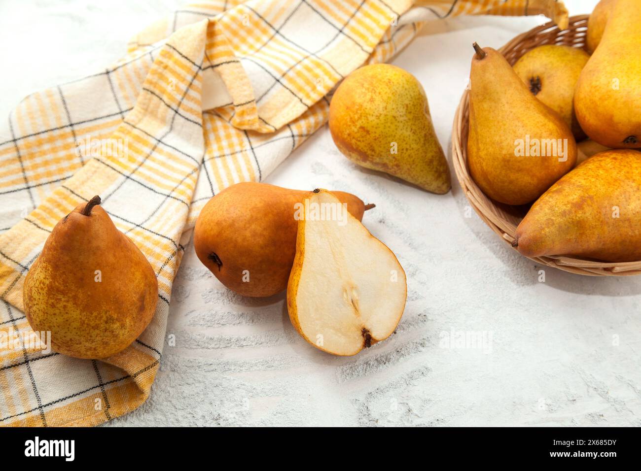 Diversi interi e metà di succosa frutta di pera matura, cesto di vimini con pere e asciugamano da cucina giallo su fondo di legno bianco. Foto Stock