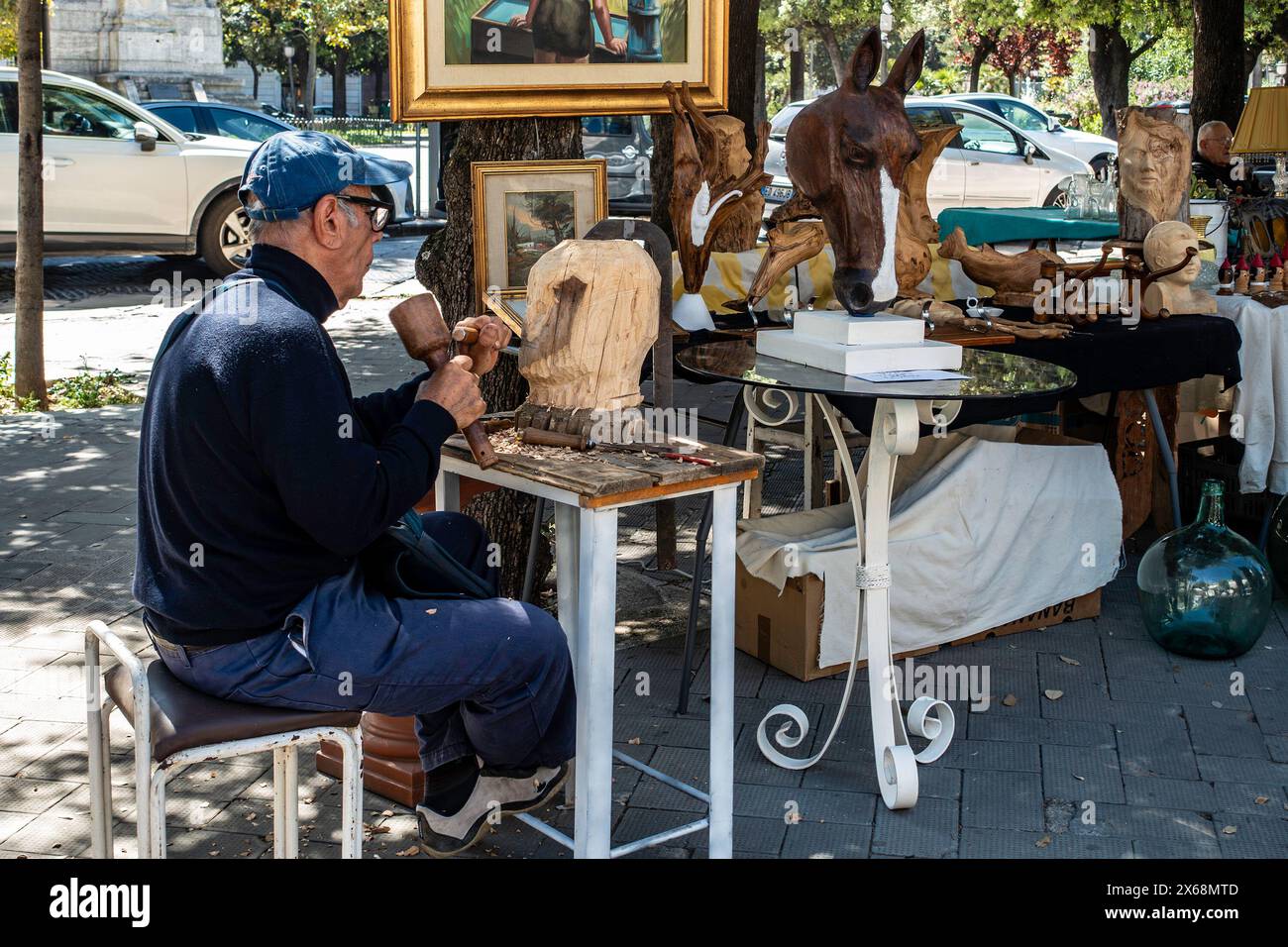 Artigiano intagliatore di legno che realizza sculture in un mercato all'aperto a Trani, Italia. Foto Stock
