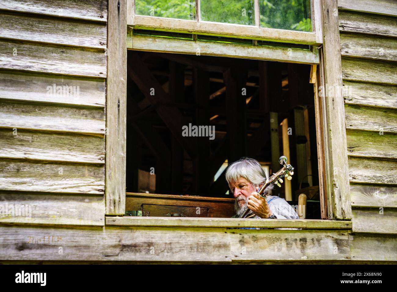 Great Smoky Mountains National Park, Mingus Mill, 12 giugno 2021: Un uomo sta suonando banjo vicino alla finestra dell'edificio storico di Mingus Mill Foto Stock