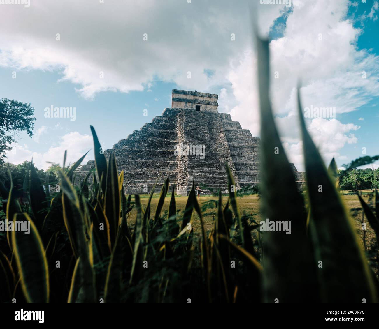 Piramide di Chichen Itza incorniciata da erba, sfondo cielo vivace Foto Stock