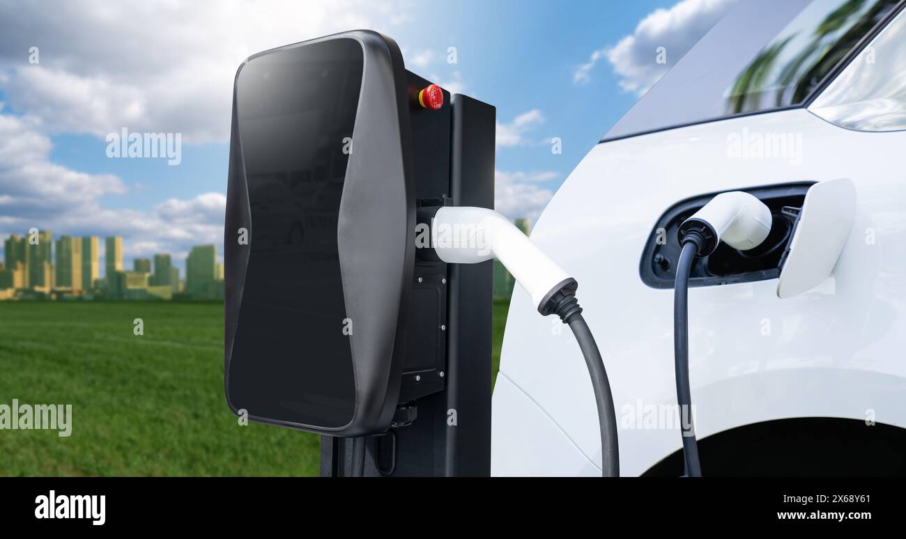 Primo piano di un'auto elettrica con un cavo di ricarica collegato sullo sfondo di una città ecologica verde. Foto Stock