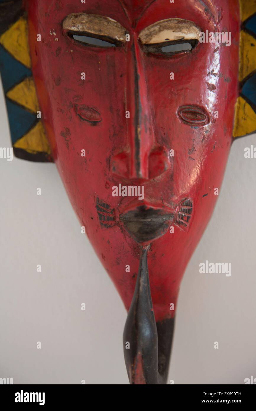 La maschera rossa di legno è appesa su una parete bianca Foto Stock