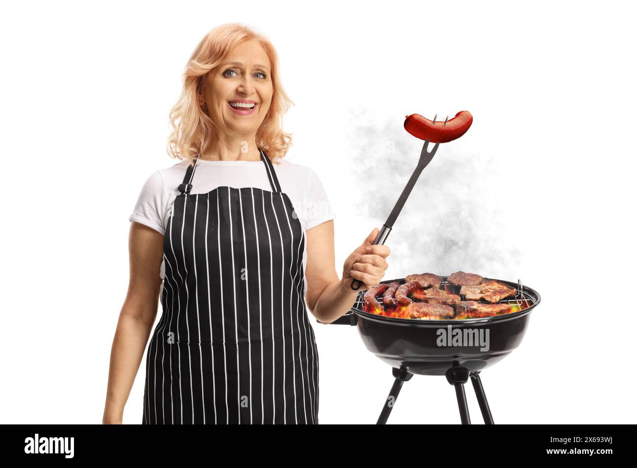 Donna che grigia la carne su un barbecue e tiene una salsiccia su una forchetta isolata su sfondo bianco Foto Stock