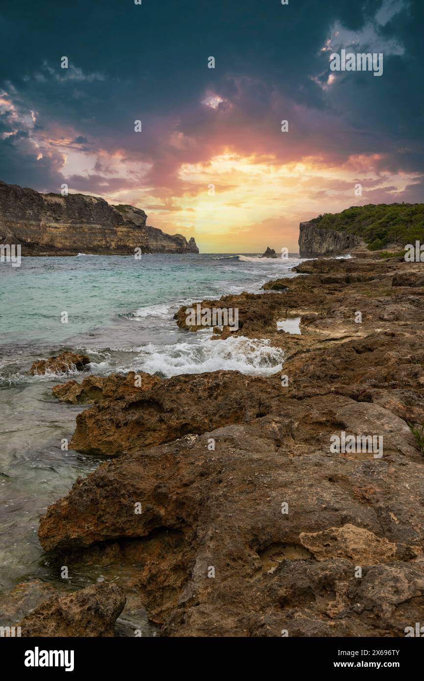 Costa rocciosa, lunga baia sul mare al tramonto. Vista pericolosa del Mar dei Caraibi. Clima tropicale al tramonto a la porte d'Enfer, grande Terre, Guadalupa, Antille francesi Foto Stock