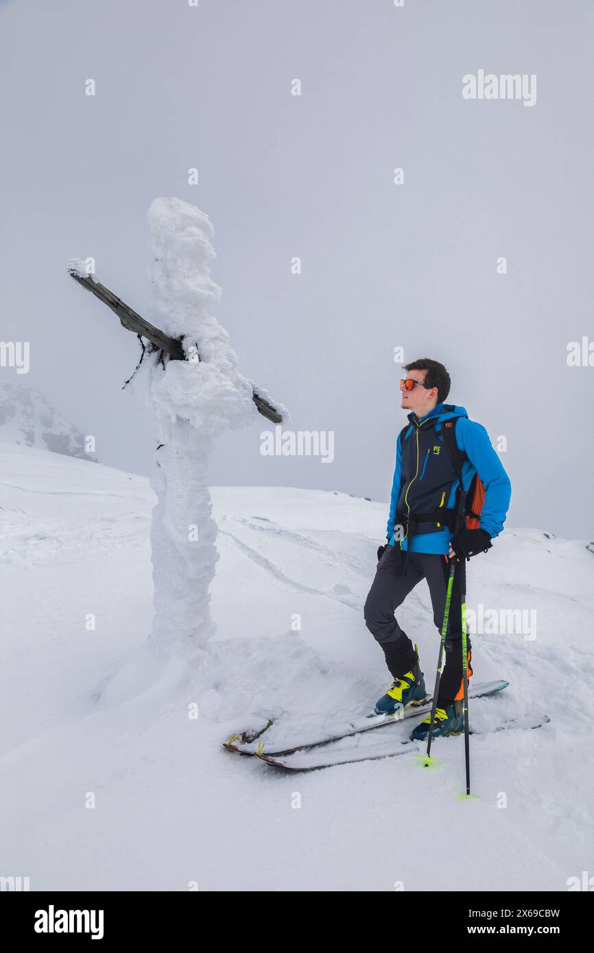 italia, Trentino, Primiero San Martino di Castrozza, scialpinista vicino ad una croce completamente ricoperta di neve ghiacciata vicino alla vetta del Juribrutto, Dolomiti Foto Stock
