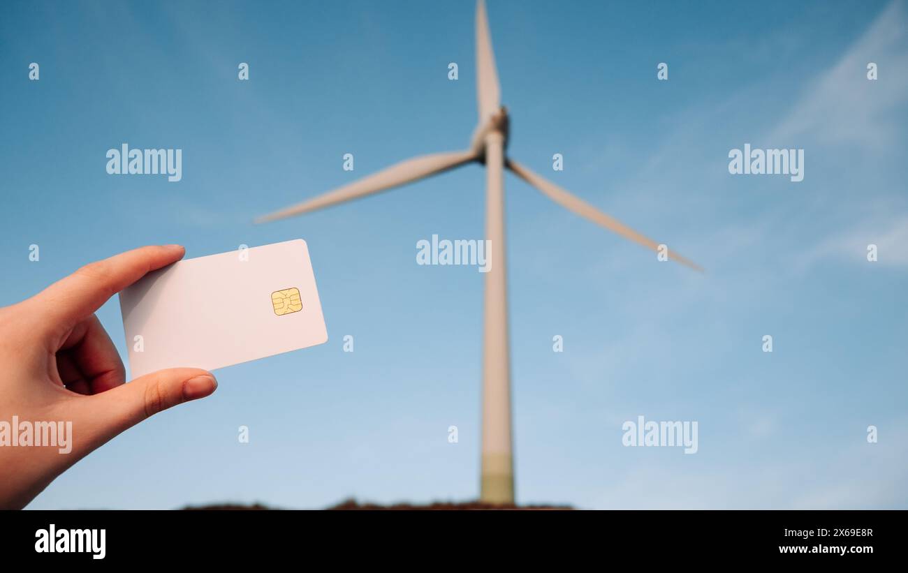 Una persona che ha una carta di credito accanto a una turbina eolica Foto Stock