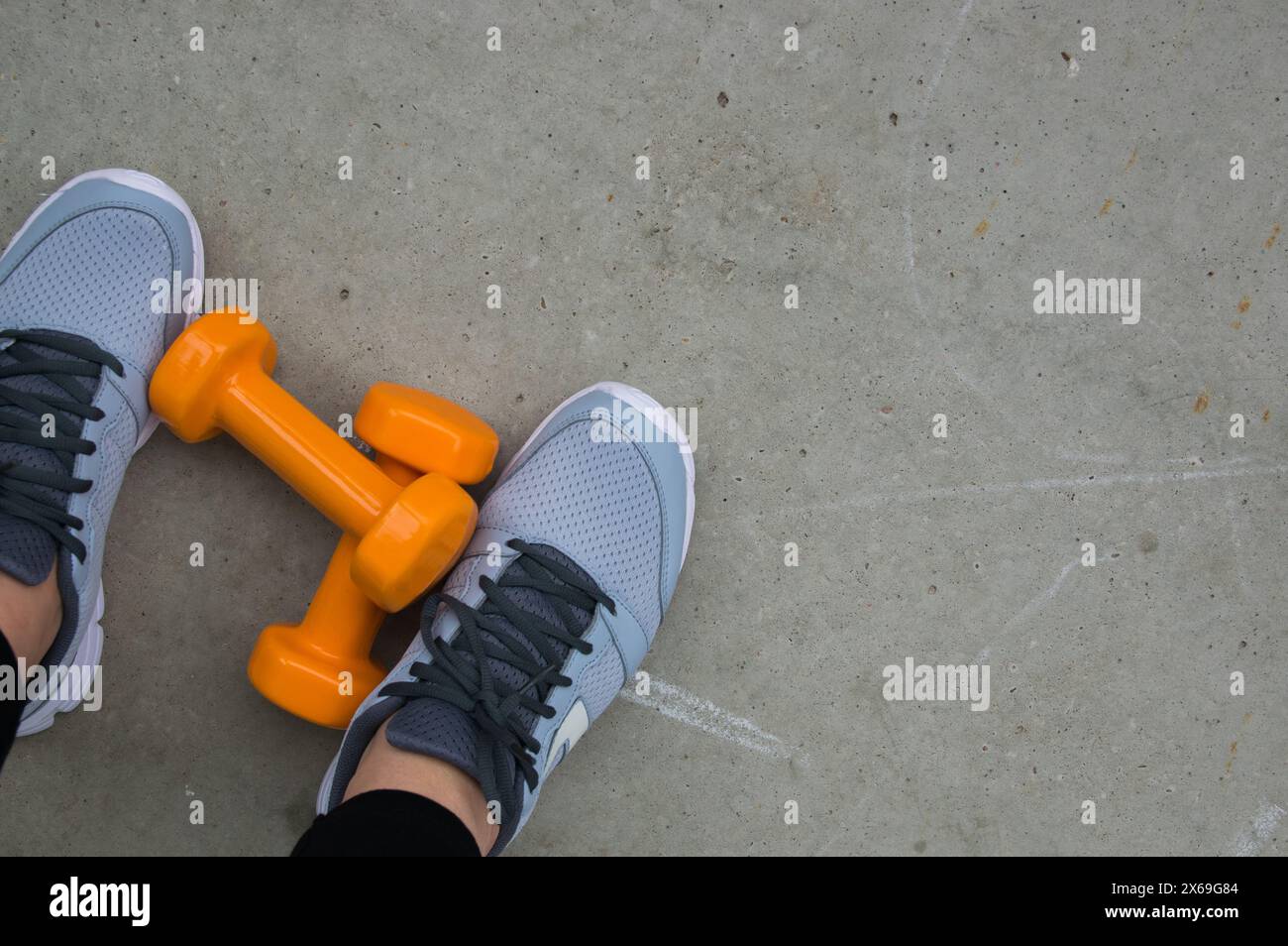 Concetto di fitness. Gambe femminili in scarpe sportive a terra con manubri. Spazio per il testo. Foto Stock