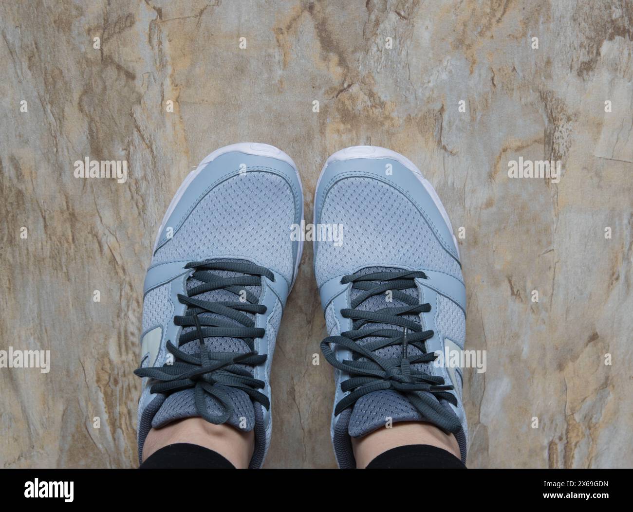 Concetto di fitness. Gambe femminili in scarpe sportive sul pavimento in marmo. Foto Stock