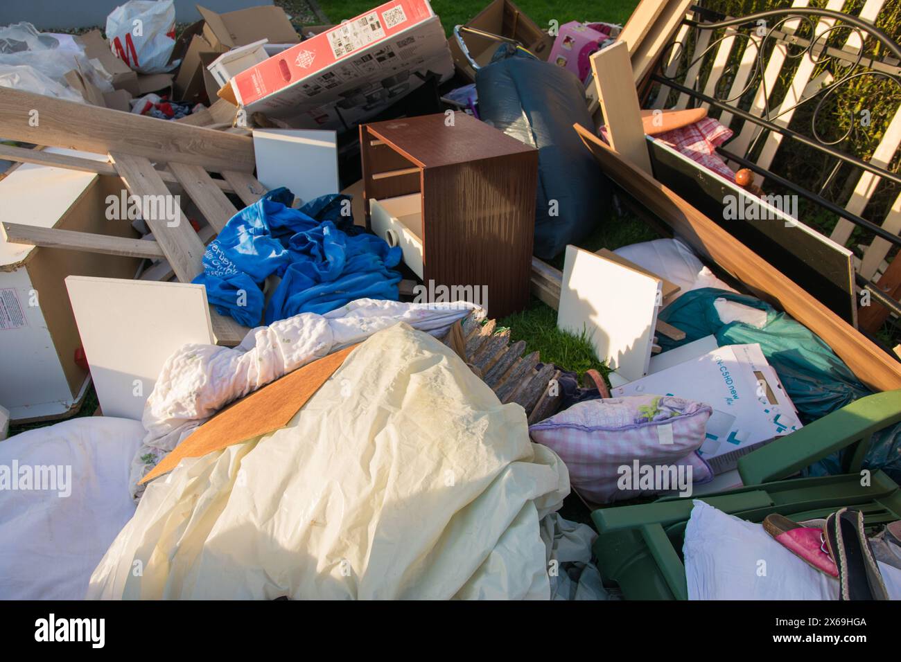 Un sacco di sprechi in una città vicino alla casa. Grande spazzatura con vecchi mobili in legno, giocattoli, scatole, sacchetti di plastica su una strada e erba verde in primavera soleggiata tra Foto Stock