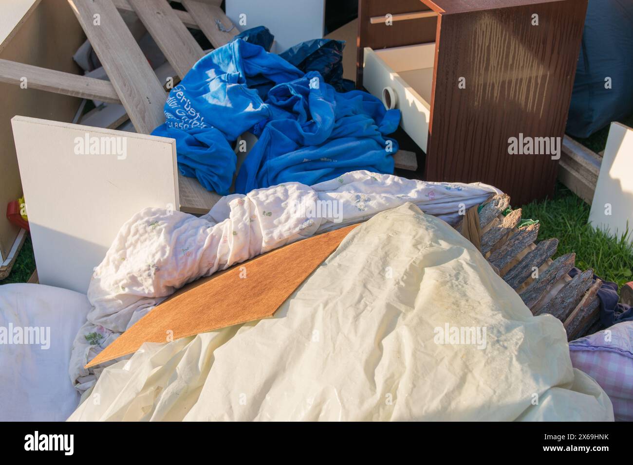 Un sacco di sprechi in una città vicino alla casa. Grande spazzatura con vecchi mobili in legno, giocattoli, scatole, sacchetti di plastica su una strada e erba verde in primavera soleggiata tra Foto Stock
