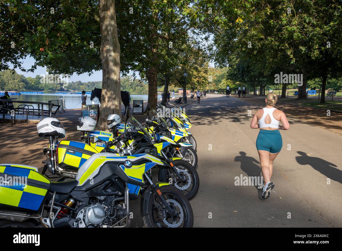 Hyde Park London, motociclette della polizia metropolitana parcheggiate all'esterno del caffè al Serpentine mentre una donna bionda fa jogging e passa oltre, Inghilterra, Regno Unito, 2023 Foto Stock