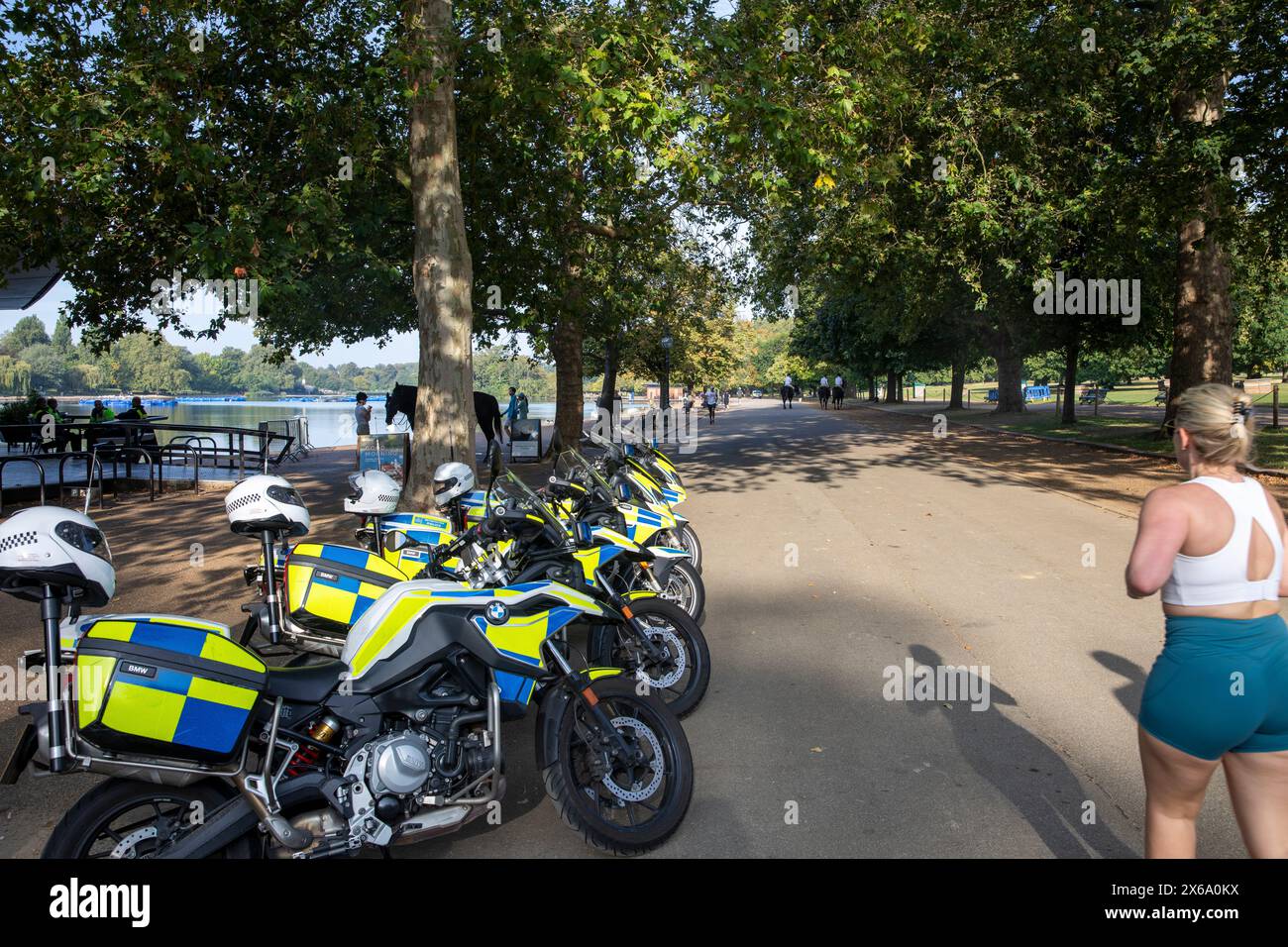 Hyde Park London, motociclette della polizia metropolitana parcheggiate all'esterno del caffè al Serpentine mentre una donna bionda fa jogging e passa oltre, Inghilterra, Regno Unito, 2023 Foto Stock
