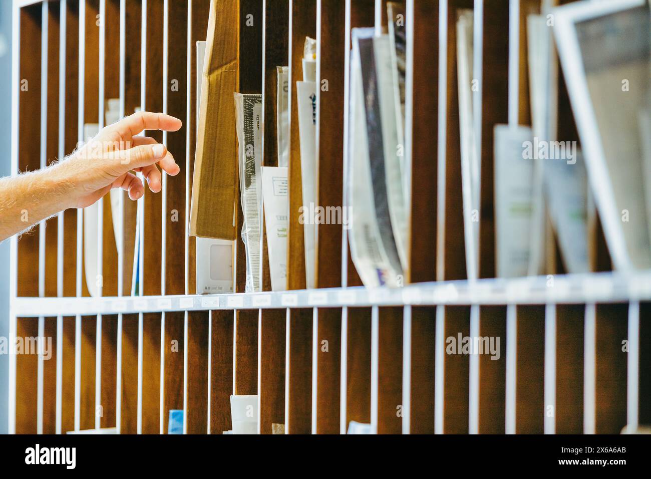 la mano di un anziano arriva in un organizzatore di posta in legno, selezionando una busta tra le numerose fessure piene di documenti e documenti. La S Foto Stock