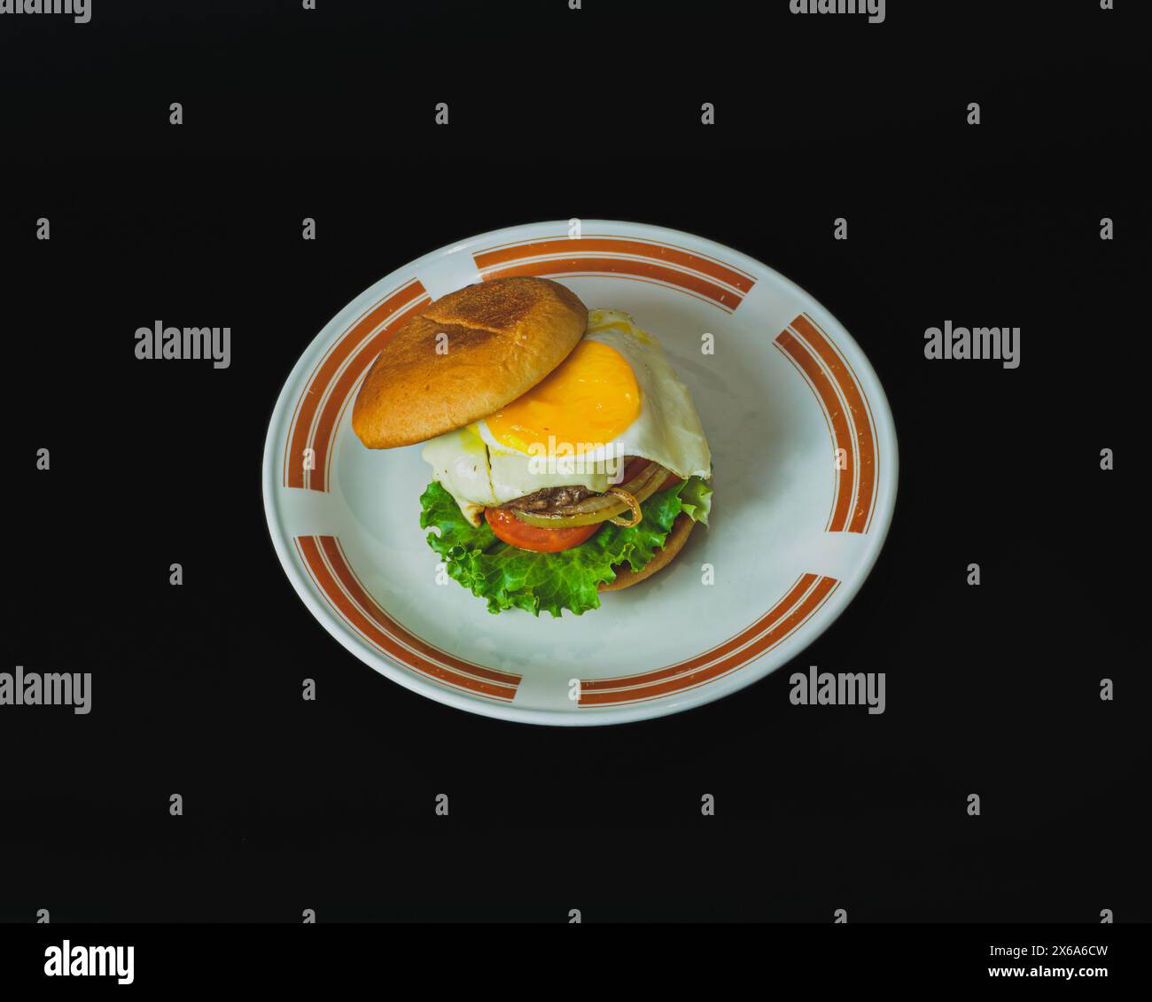 Una succosa polpetta di hamburger fatta in casa condita da un uovo fritto con un lato soleggiato. L'hamburger è su un piatto bianco. Foto Stock