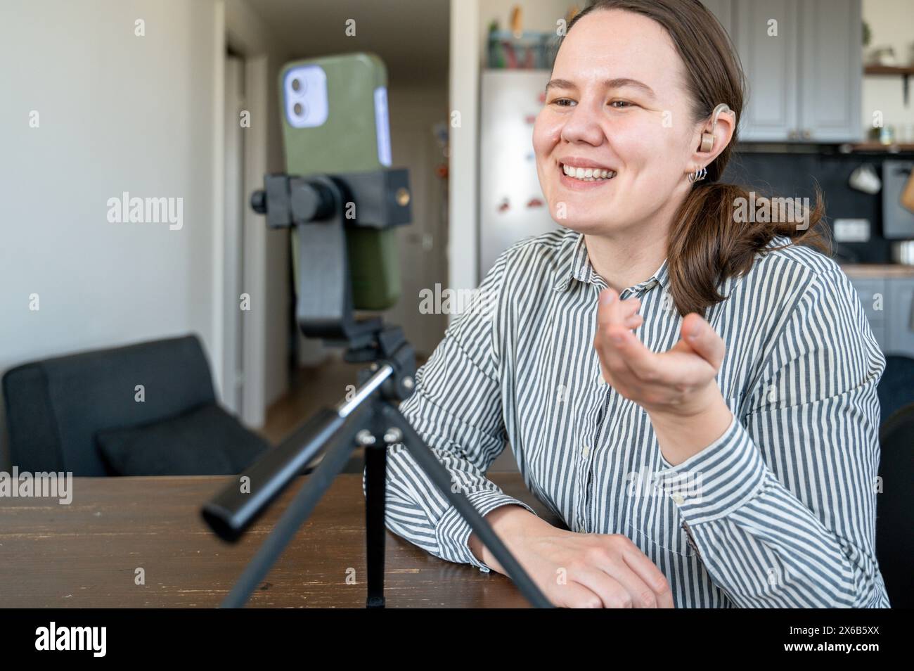 Ritratto di una giovane donna sorridente con l'apparecchio acustico sull'orecchio sinistro per registrare video o videochiamare a casa Foto Stock