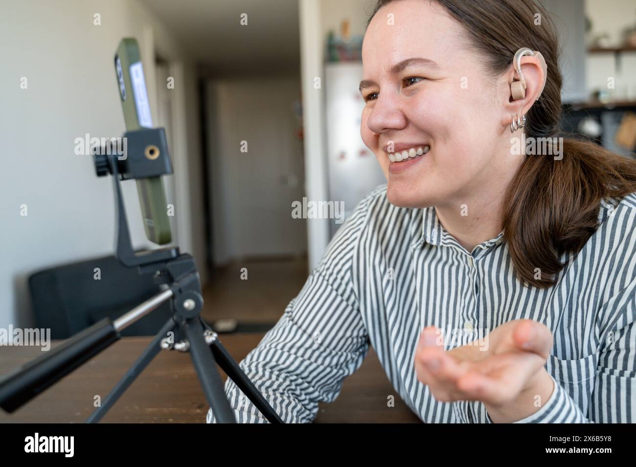 Ritratto di una giovane donna sorridente con l'apparecchio acustico sull'orecchio sinistro per registrare video o videochiamare a casa Foto Stock