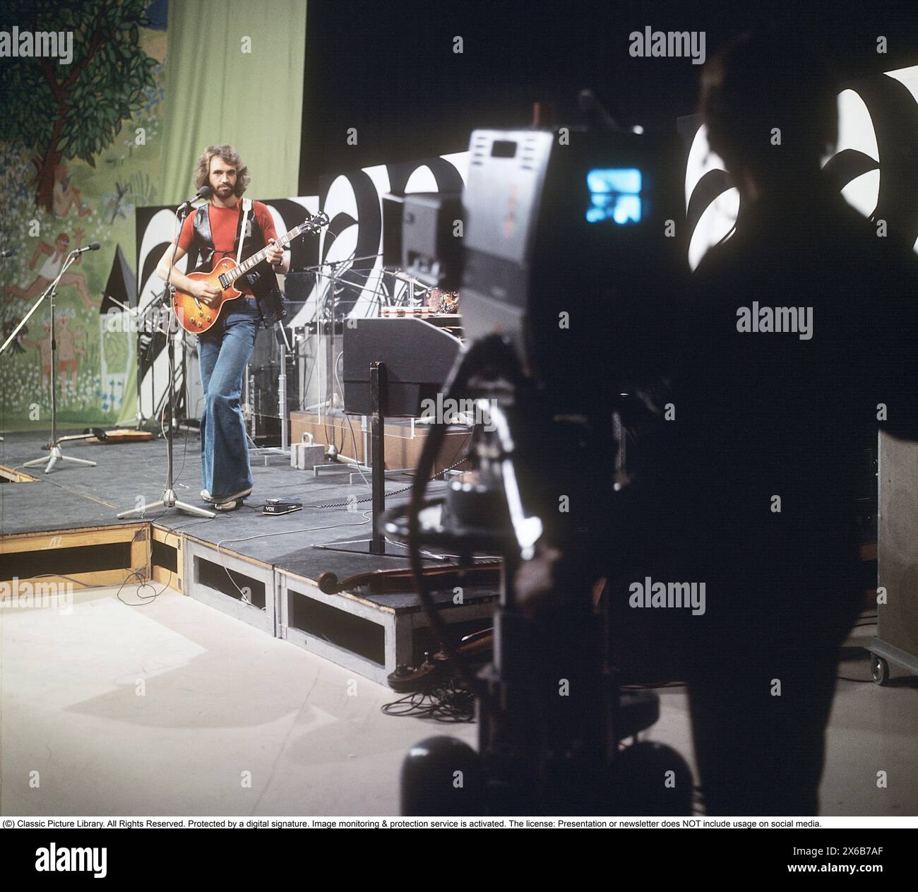 Moda degli anni '1970 Un giovane uomo che indossa la tipica moda degli anni '1970, pantaloni a gambe larghe. Uno stile chiamato campana o zampe, pantaloni che si allargano dalle ginocchia e verso il basso, formando una forma a campana della gamba dei pantaloni. È il musicista Claes af Geijerstam con la sua band Marsfolket in uno studio televisivo che registra un programma. 1971. Svahn Foto Stock