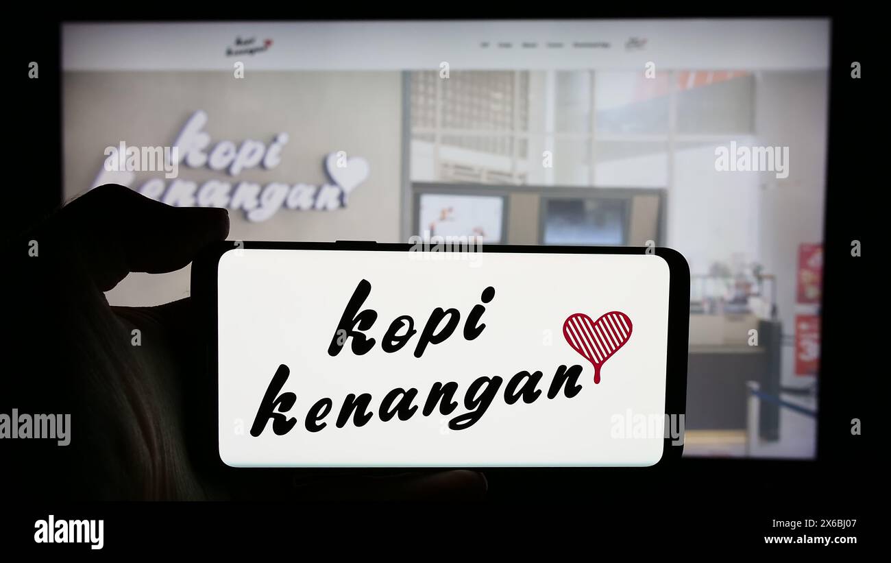 Persona che detiene un cellulare con il logo della catena di caffè indonesiana Kopi Kenangan di fronte alla pagina web aziendale. Mettere a fuoco il display del telefono. Foto Stock