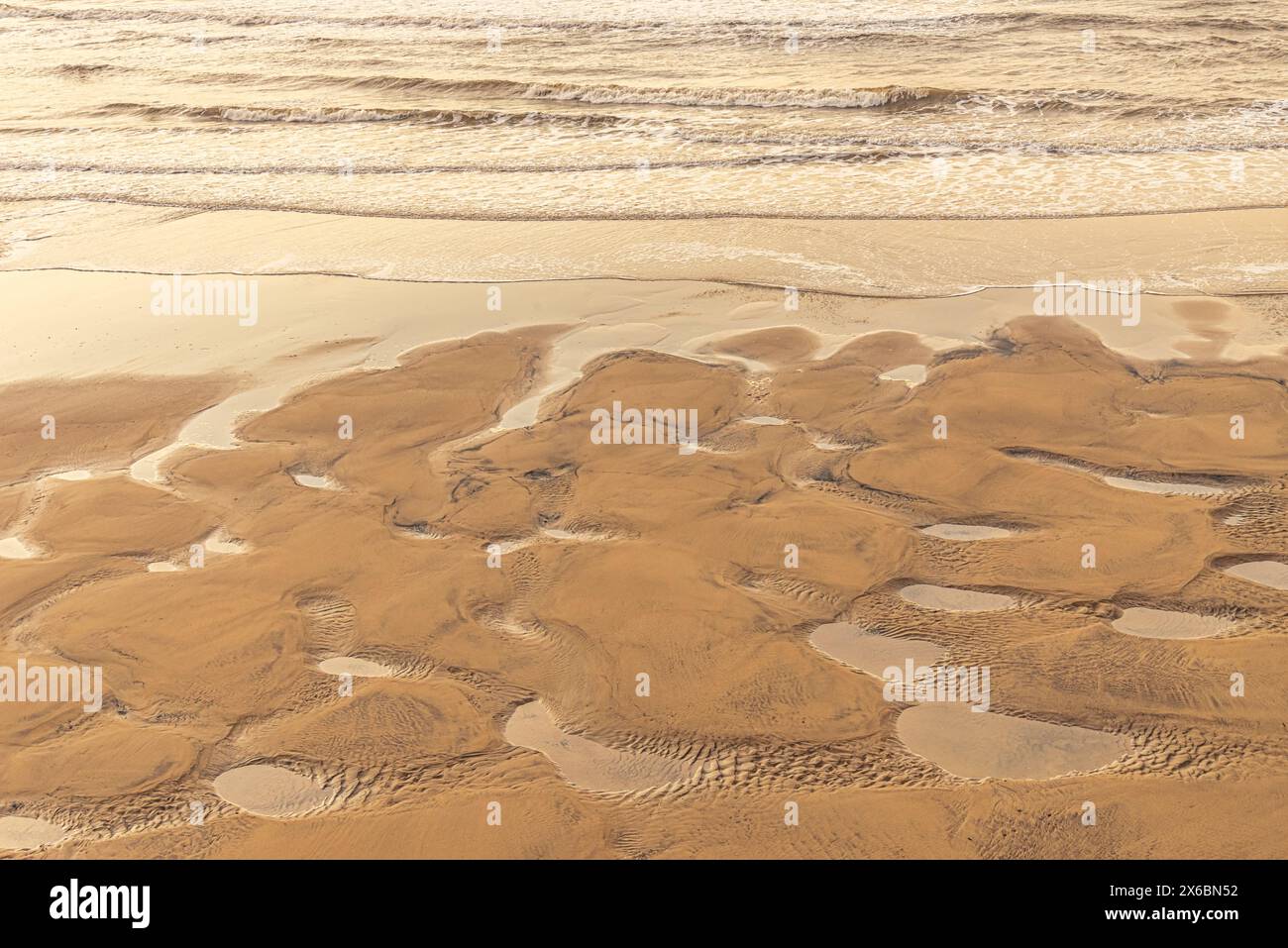 Motivi lasciati nella sabbia con pozze d'acqua dopo una marea di neap su una spiaggia. Le onde rotolano verso la riva. Foto Stock